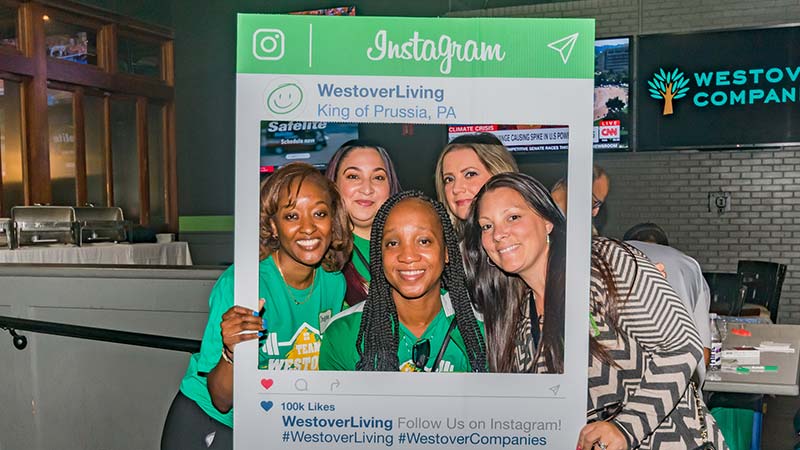 Westover employees at a social event posing with an Instagram photo booth prop