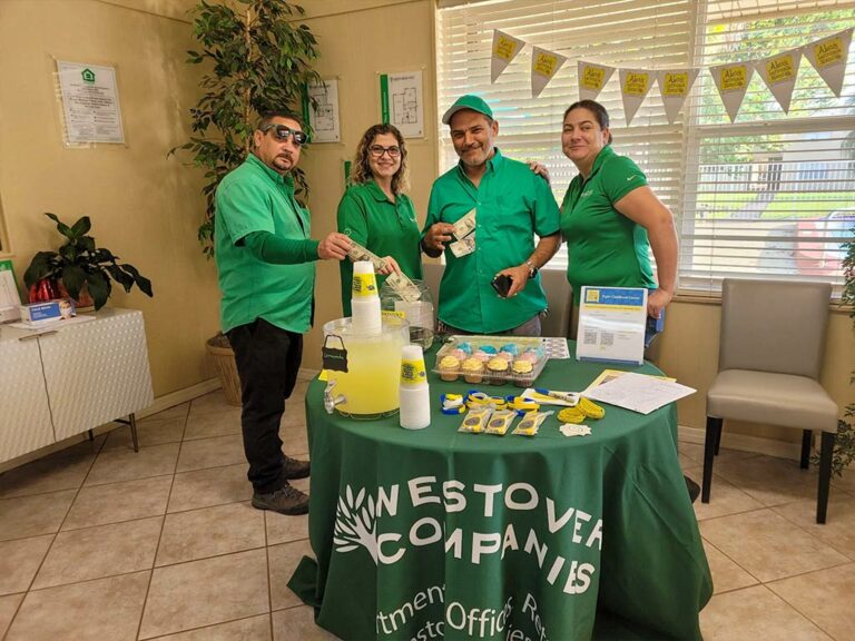Volunteers posing for a photo at a table with lemonade and cupcakes